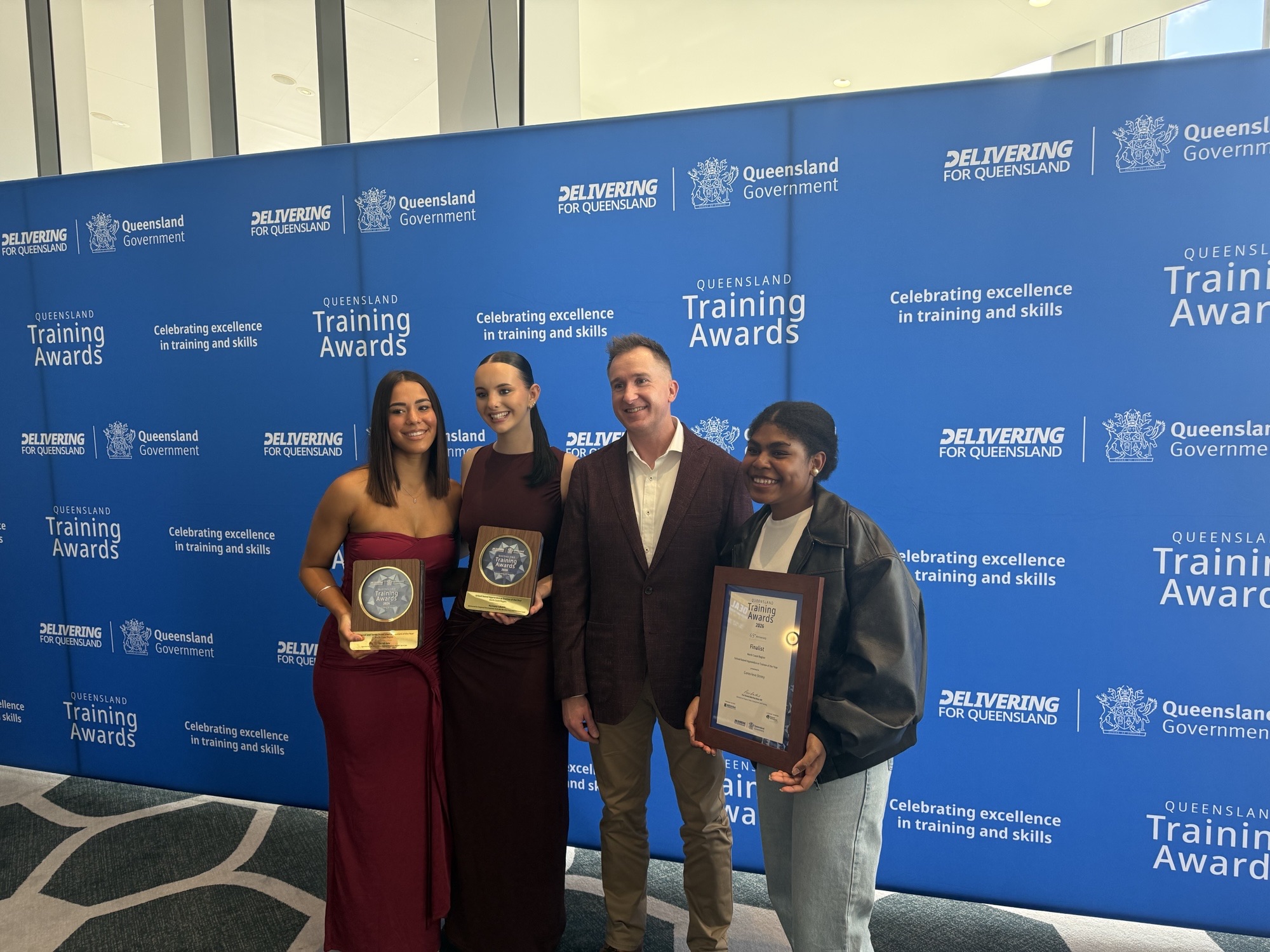 Taylah Gela, Harmony Lakatos, SWC trainer Brad Lowe and Genevieve Jimmy holding their awards in front of the Queensland Training Awards media wall